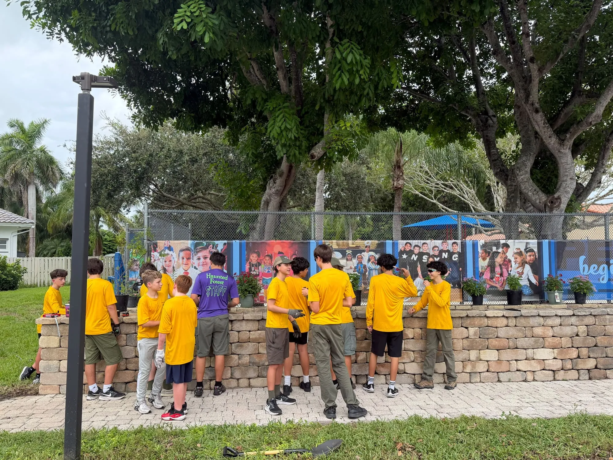 Scouts in yellow shirts work along a low stone wall, planting in a row of pots.