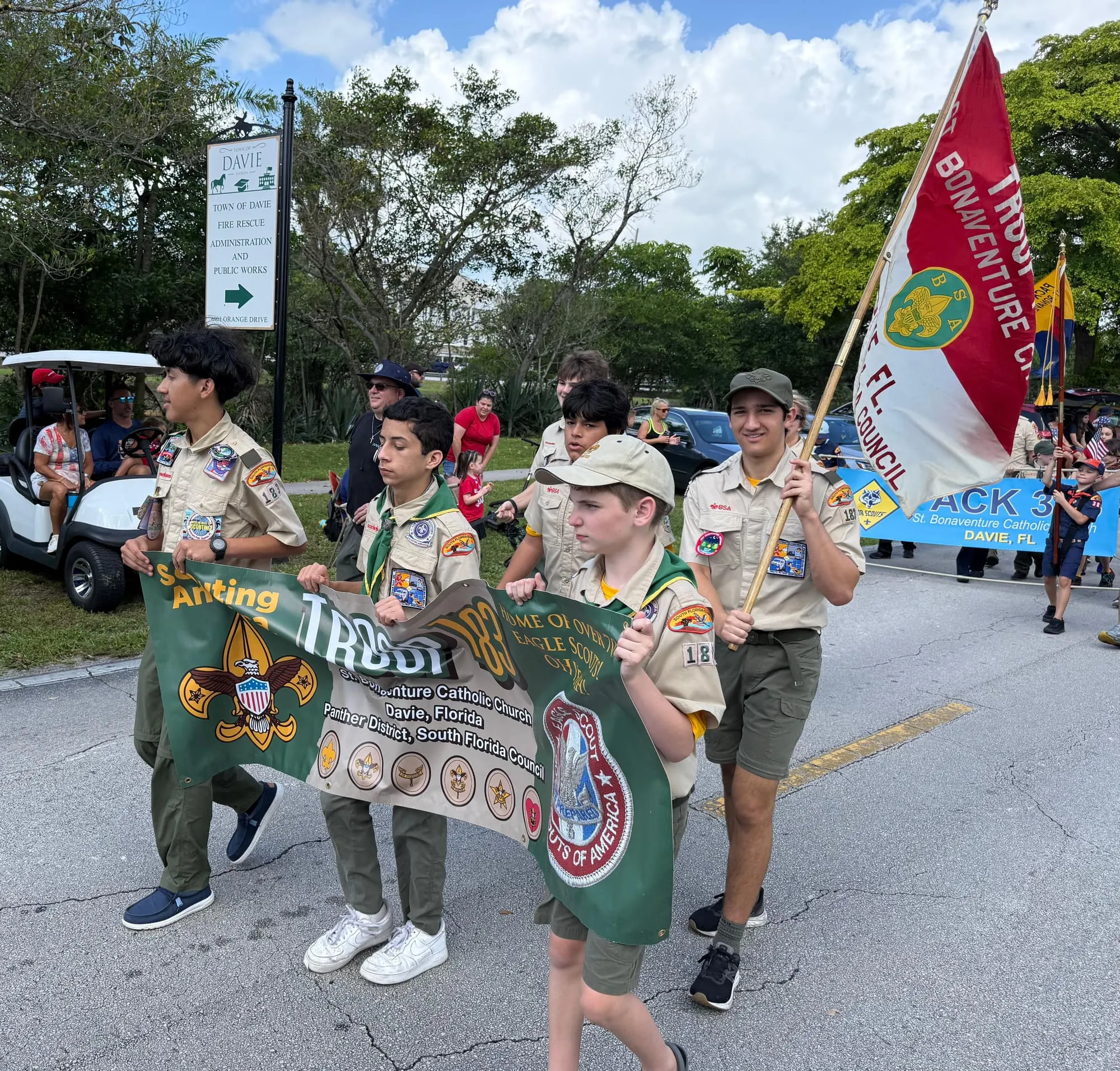 Scouts in uniform carry the Troop 183 banner along a street in Davie.