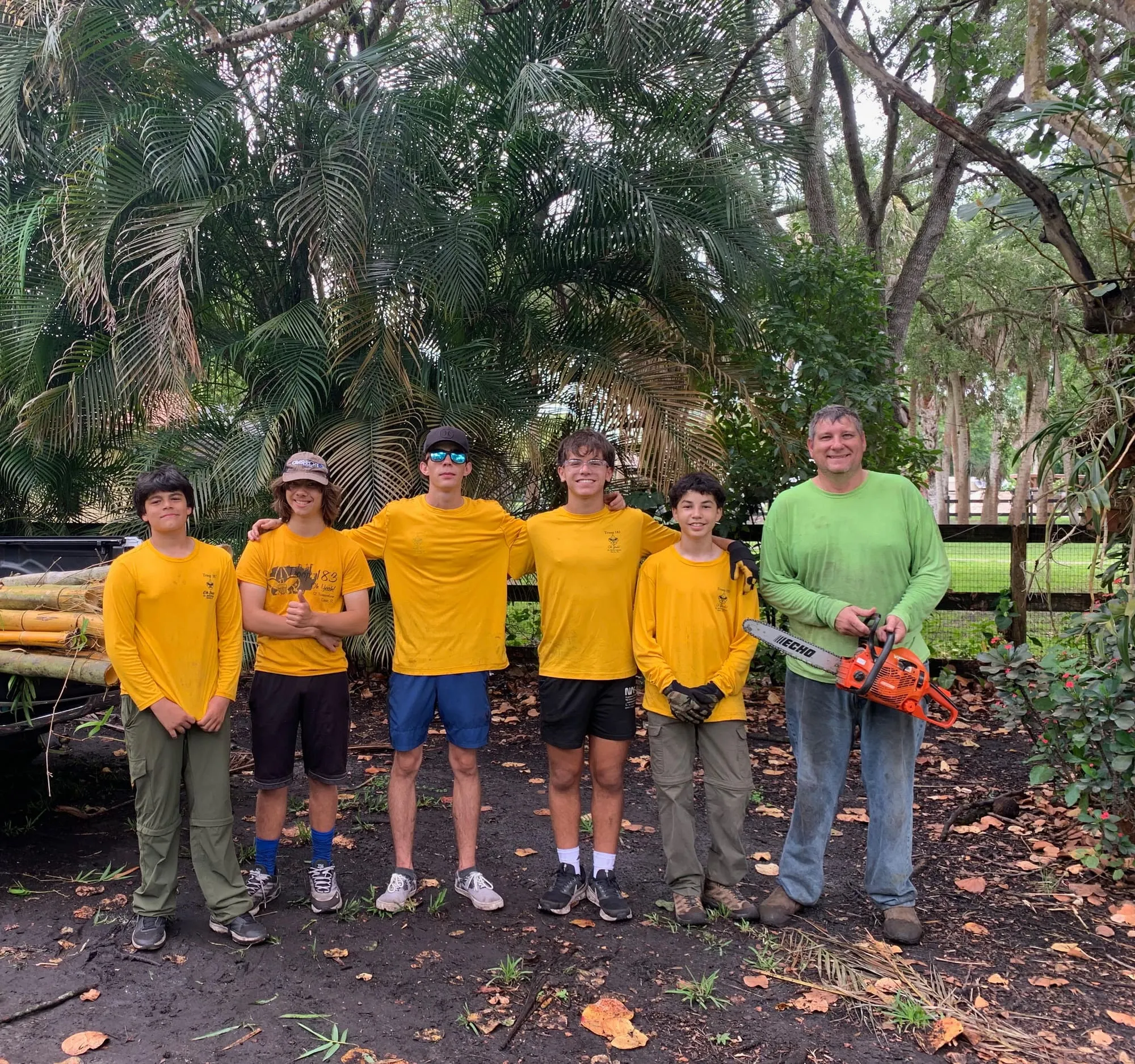 Scouts stand with an adult leader after a brush-clearing service project.